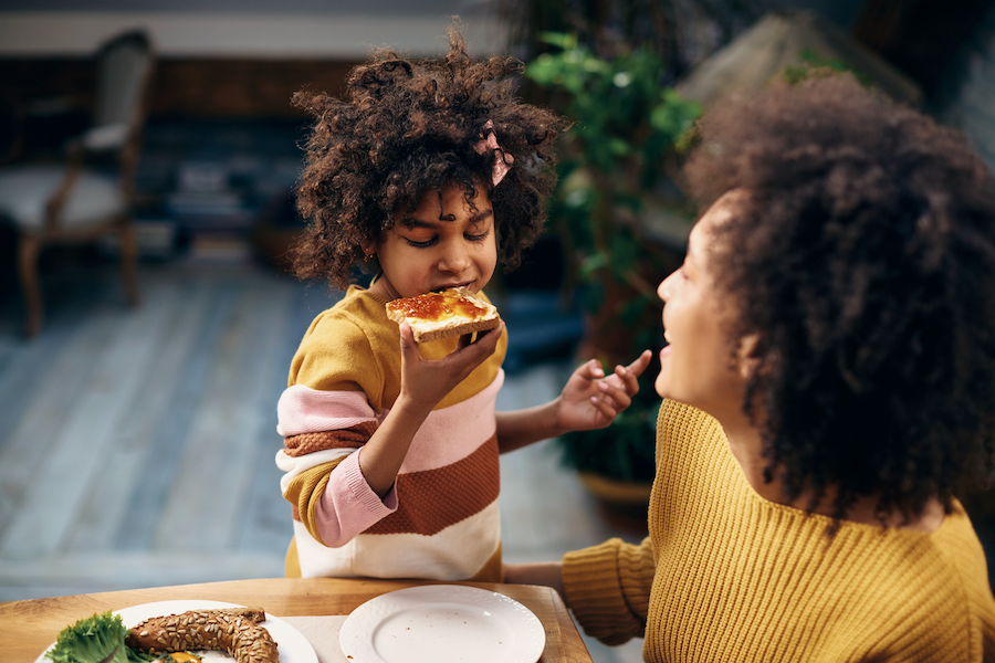 child eating toast while her mother looks on