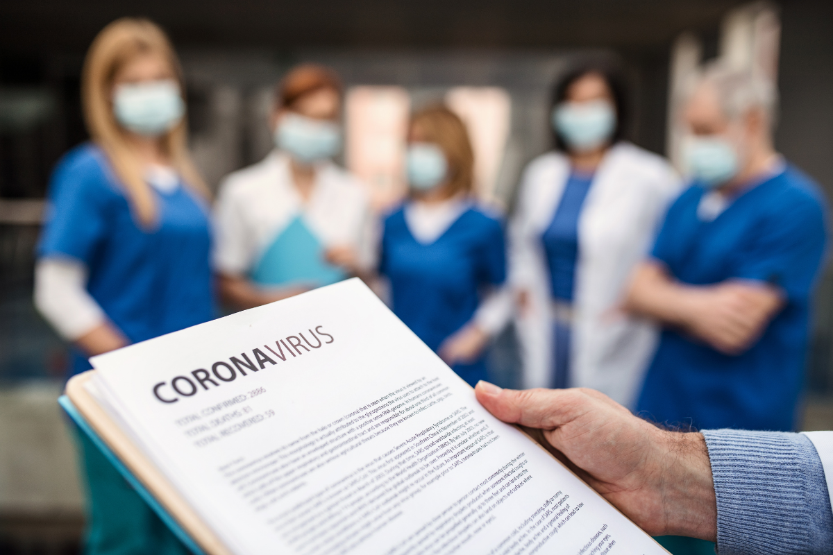 Doctors standing in masks while one holds a paper that says Coronavirus