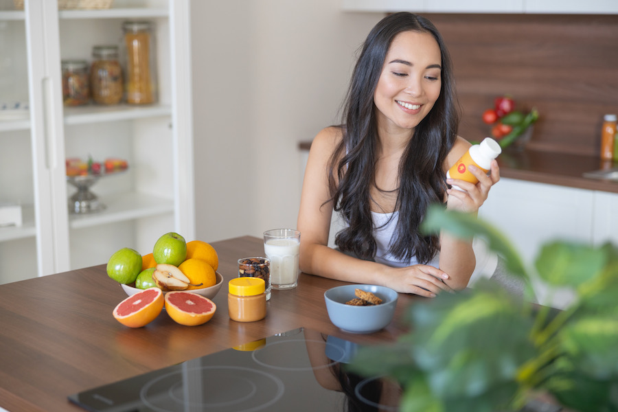 Young woman reading vitamin supplement bottle during breakfast