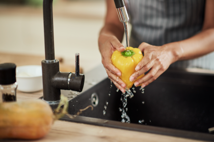 Person washing a yellow bell pepper at the sink